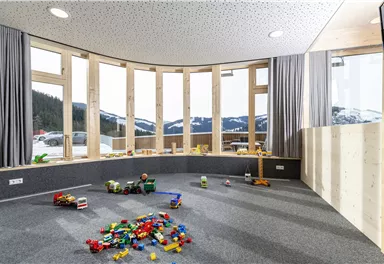 A bright playroom with large windows and a view of the mountains. Colorful toys are laid out on the floor, creating an inviting atmosphere for children.
