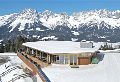 A modern building in the mountains, surrounded by snow-covered peaks. The terrace offers a beautiful view of the alpine landscape.