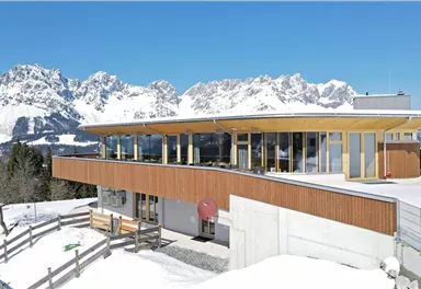 A modern building in the mountains, surrounded by snow-covered landscapes. In the background, impressive mountain peaks can be seen under a clear blue sky.