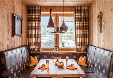 Ein gemütlicher Restaurantbereich mit Holzverkleidungen und einem großen Tisch. Auf dem Tisch stehen kleine Teller mit Speisen und zwei Gläser Bier.