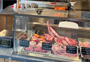 A meat stand with various types of meat behind a glass display. Clearly visible price tags indicate the products.