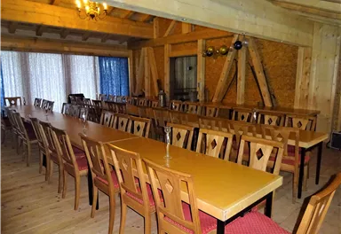A large dining room with long tables and wooden chairs. The walls are made of wood and large windows let in a lot of light.