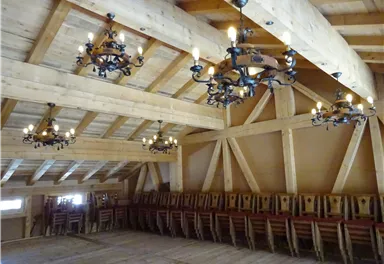A cozy room with wooden ceilings and several chandeliers. On the left side, stacked chairs can be seen.