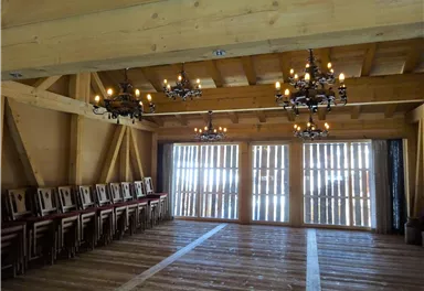 A spacious room with wooden beams and hardwood flooring. The room is fitted with chandeliers and a large window front.