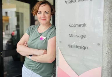 A woman stands in front of the "Violet Beauty" sign. The sign displays offers such as cosmetics, massage, and nail design.