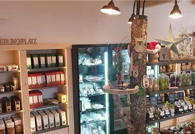 Ein gemütlicher Laden mit Regalen voller Tees, Gewürze und anderen Produkten. In der Mitte steht ein Kühlschrank mit Drinks und verschiedenen Leckereien.