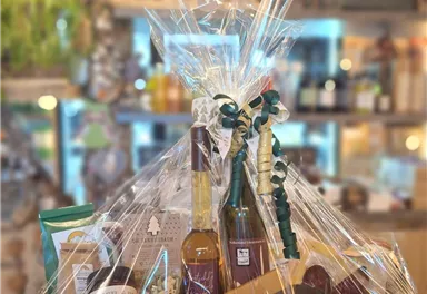 A gift basket with various delicacies and beverages, beautifully packaged in cellophane. The basket includes liqueurs, sweet treats, and snacks.