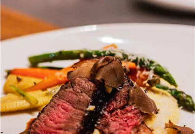 Ein Teller mit saftigem Steak, begleitet von buntem Gemüse und cremigem Püree. Das Gericht ist kunstvoll angerichtet und sieht appetitlich aus.