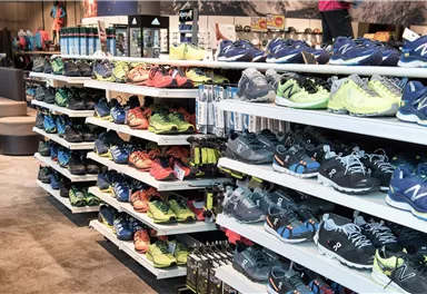 Ein Geschäft mit einer großen Auswahl an Sportschuhen auf Regalen. Die Schuhe sind in verschiedenen Farben und Stilen angeordnet.