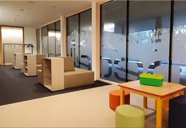 A bright room with modern furniture and game tables. In the corner, there are colorful chairs and a table with building blocks.