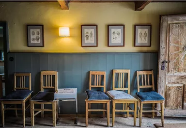 Ein gemütlicher Raum mit einer Reihe von Holzstühlen und einem rustikalen Tür. An der Wand hängen Bilder in Rahmen, und eine Lampe beleuchtet den Bereich.