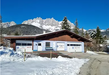 Ein gemütliches Haus im Schnee mit Garagen und einem blauen Himmel. Im Hintergrund sind die Berge sichtbar.