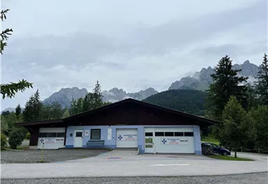 A modern building in a natural environment, surrounded by trees and mountains. The sky is cloudy and there is a calm atmosphere.