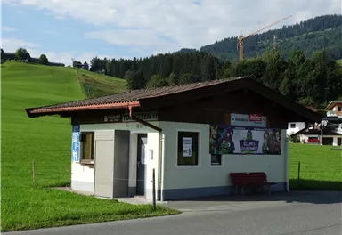 Eine kleine Verkaufsstelle am Straßenrand, umgeben von grünen Wiesen. Im Hintergrund sind sanfte Hügel und Wälder sichtbar.