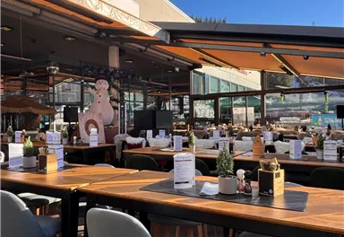 Ein modernes Restaurant mit Holzstühlen und großen Fenstern. Der Außenbereich ist hell und einladend, ideal für ein gemütliches Essen.