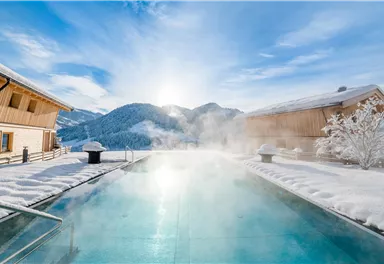 A beautiful outdoor pool surrounded by snow-capped mountains. The sun is shining, creating a relaxing atmosphere.