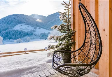 A cozy hanging swing on a balcony with a view of a snowy landscape. In the background, snow-covered mountains and trees can be seen.