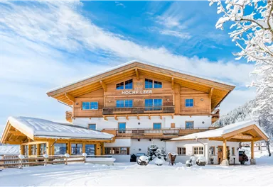 A picturesque wooden house in the snow with large windows and a balcony. The clear sky and the winter landscape give the scene a cozy atmosphere.