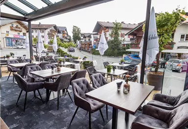 Ein modernes Café mit gemütlichen Tischen und Stühlen. Die großen Fenster bieten einen Blick auf die Stadt und die umliegenden Berge.