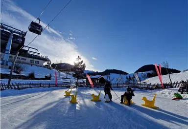 Ein schneebedecktes Gelände mit einer Seilbahn und bunten Figuren in Form von Tieren. Im Hintergrund sind Hügel und ein klarer blauer Himmel zu sehen.
