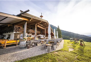 A rustic restaurant in the midst of the mountains with an inviting terrace. The surrounding landscape is green and picturesque.