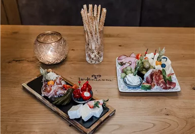An appealing selection of antipasti on wooden boards, garnished with fresh vegetables and cold cuts. In the background, there is a candle holder with a tealight and grissini.