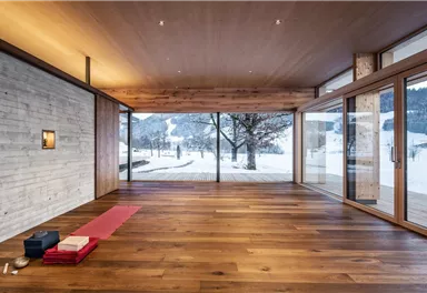 Ein moderner Raum mit großen Fenstern und Holzfußboden. Draußen ist eine winterliche Landschaft mit Schnee zu sehen.