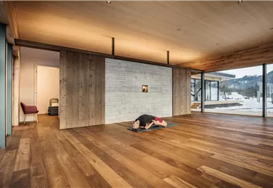 Ein modernes Yoga-Studio mit Holzfußboden und großen Fenstern. Eine Person praktiziert Yoga in einer ruhigen Umgebung mit Blick auf die Natur.