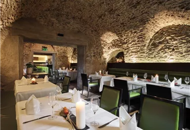 An elegant restaurant with stone walls and soft lighting. The tables are lavishly set and invite you to linger.