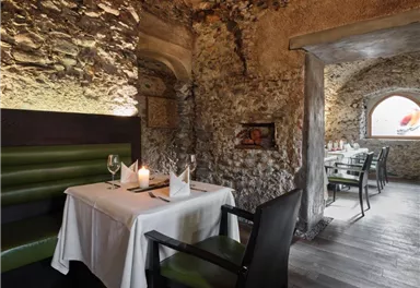 A cozy restaurant with stone walls and elegant tables. Green seats and soft lighting create an inviting atmosphere.