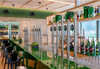 Eine elegante Bar mit grünen Elementen und einem langen Bartresen. Im Hintergrund sind verschiedene Getränke und Gläser sichtbar.