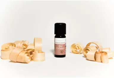 A bottle of essential oil stands in the center, surrounded by wood shavings. The oil is packaged in a black vial and appears to be intended for aromatic purposes.