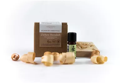 A set of cedar-scented products, consisting of a small bottle of essential oil and a decorative box. Wood shavings are scattered around the products.