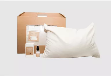 A set with a cushion, a box, and care products. The packaging is made of brown cardboard and the products are in neutral colors.