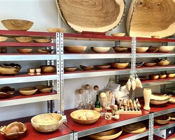 A shelf with various handcrafted wooden bowls and objects. The exhibits showcase the natural grain of the wood and vary in shape and size.