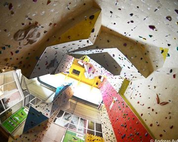 Eine Kletterhalle mit bunten Kletterwänden und vielen Griffen. Die Decke ist hoch und bietet verschiedene Routen für Kletterer.