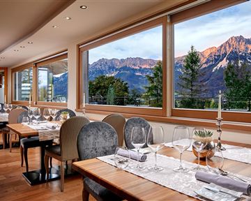 Ein elegantes Restaurant mit Holztischen und stilvollen Stühlen. Die großen Fenster bieten einen Blick auf majestätische Berge und eine schöne Landschaft.