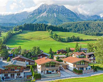 Eine malerische Landschaft mit charmanten Häusern und üppigen, grünen Wiesen. Im Hintergrund erhebt sich ein majestätischer Berg unter einem hellen Himmel.