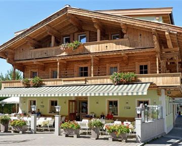 A rustic wooden building with a balcony and many flowers. There are outdoor seating options in front of the house.