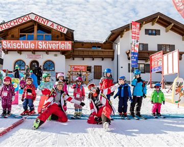 A ski school with a colorful building in the background. In front of the building, ski instructors and children in ski clothing are standing on snow.