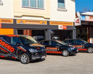 Three vehicles with eye-catching advertisements are parked in front of a store with an orange and white sign. The store offers services and has large windows.