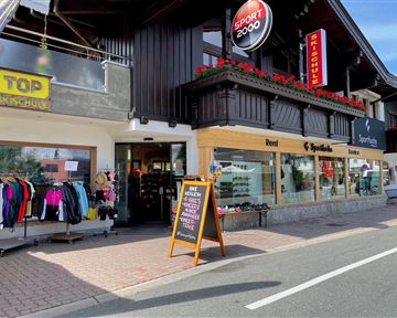Ein Sportgeschäft mit einer großen Auswahl an Sportkleidung und Ausrüstung. Die Fassade ist mit Blumen dekoriert und es gibt ein Schild, das auf besondere Angebote hinweist.