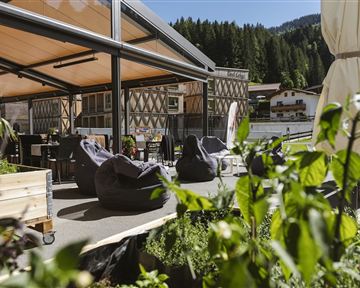 Eine gemütliche Terrasse mit Sitzsäcken und Blick auf die umliegenden Berge. Grüne Pflanzen umgeben den Bereich und sorgen für eine entspannte Atmosphäre.