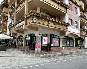A modern building with a shop on the ground floor. The windows display colorful advertisements and there is an outdoor terrace.