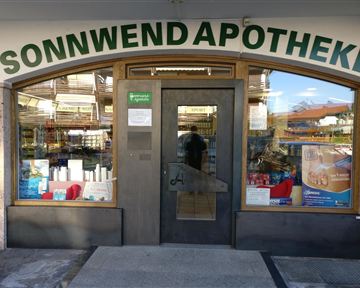 Eine Apotheke namens Sonnwend mit einem einladenden Eingang. Im Fenster sind verschiedene Produkte sichtbar.