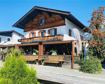 Ein charmantes Holzhaus mit einer einladenden Terrasse. Umgeben von grünen Pflanzen und einem blauen Himmel.