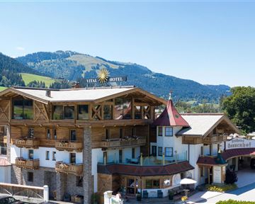 Ein charmantes Hotel im alpinen Stil mit Holzverkleidung. Die Umgebung bietet eine beeindruckende Bergkulisse und einen grünen Garten.