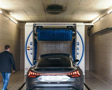A car is being washed in a car wash. A person is walking towards the vehicle.