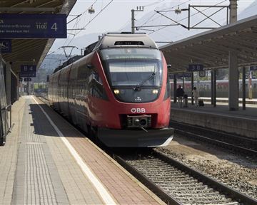 A red train is standing at the station on track 4. The surroundings are bright and well-lit, with modern platform structures.