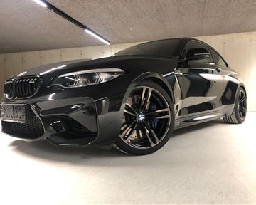 A sporty BMW in a modern parking garage. The car is black with eye-catching rims and a dynamic design.